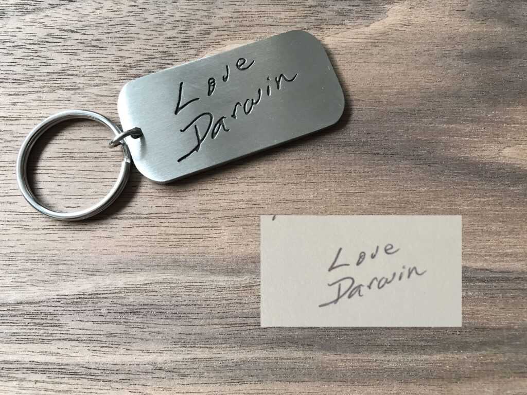 Engraved metal keychain with Love Darwin handwritten message on wooden surface.