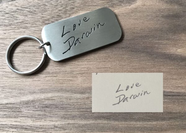 Engraved metal keychain with Love Darwin handwritten message on wooden surface.
