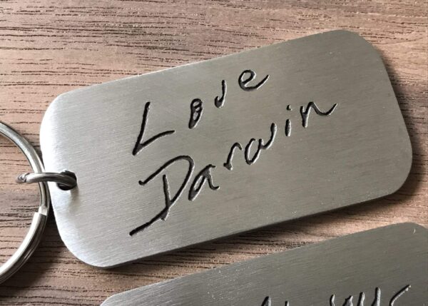 Etched metal keychain with Love Darwin inscription on a wooden surface.