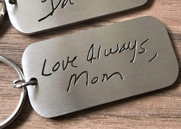 Engraved metal keychain with handwritten message Love Always, Mom on a wooden surface.