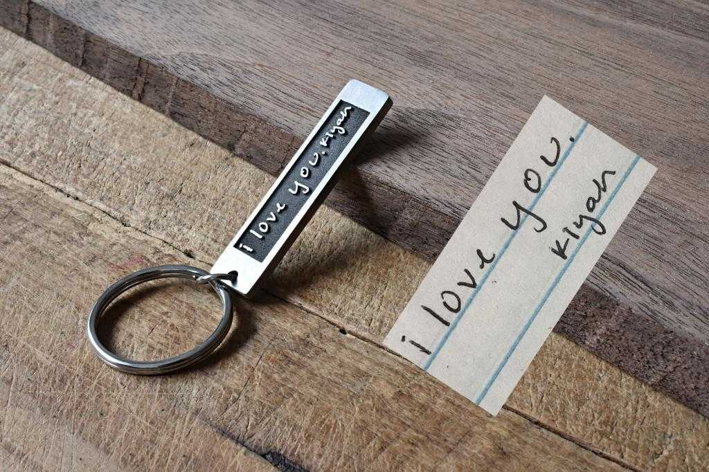 Keychain with engraved I Love You message beside handwritten note on wooden surface. Romantic gift concept.