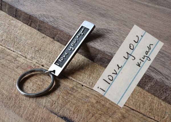Keychain with engraved I Love You message beside handwritten note on wooden surface. Romantic gift concept.