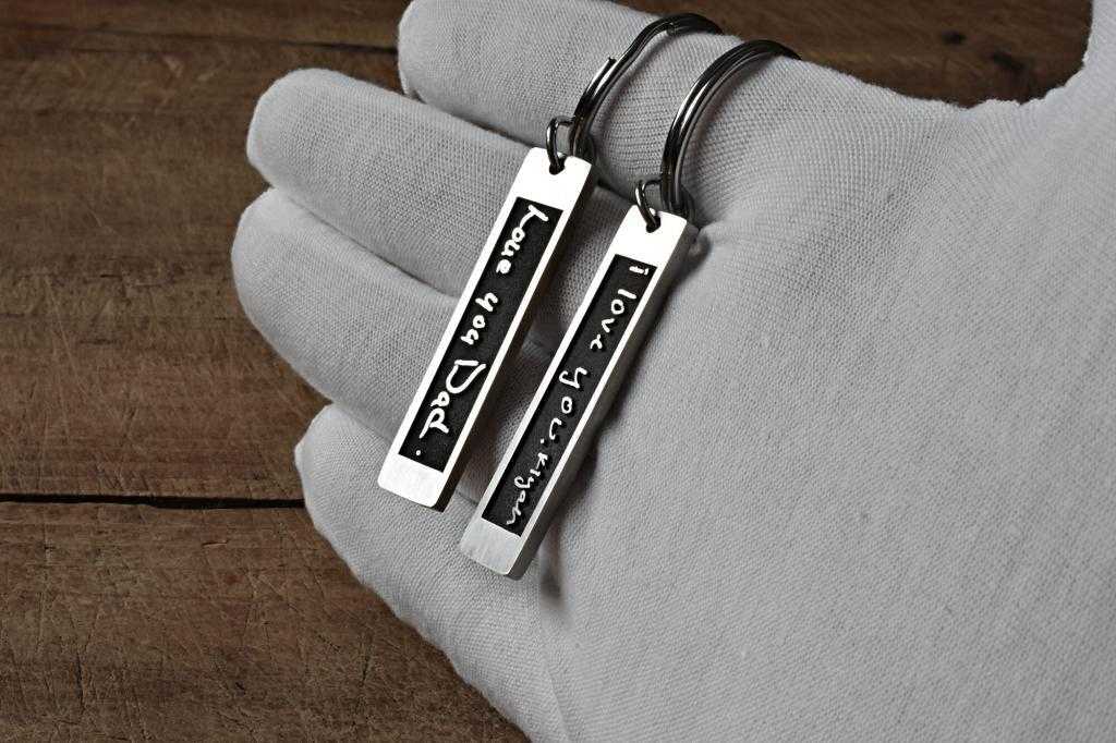 Engraved silver keychains saying I love you Dad and I love you heaps on a gloved hand.