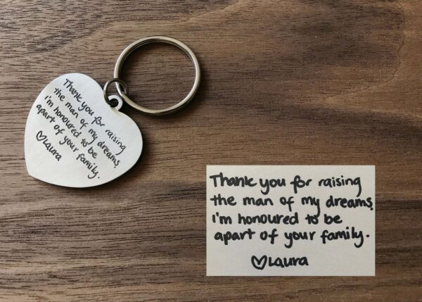 Heart-shaped keychain with heartfelt thank you message from Laura to a family, alongside a handwritten note on wood.