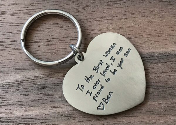 Heart-shaped keychain with engraved message from son to mother on a wooden surface. Perfect sentimental gift.