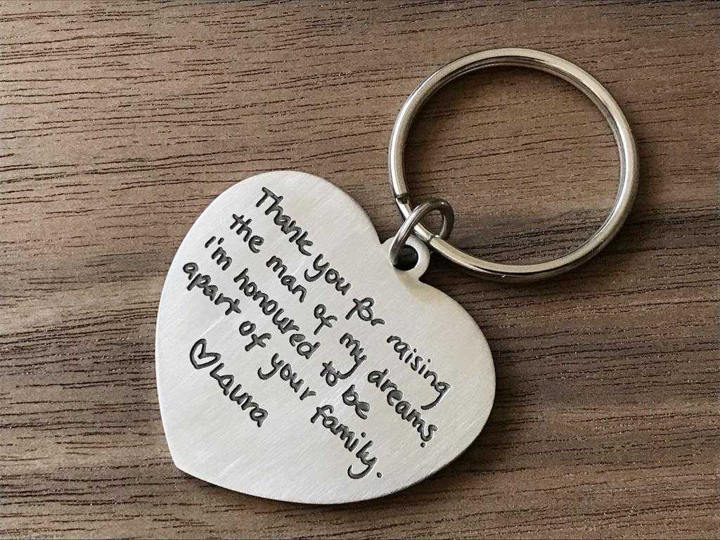 Heart-shaped keychain with engraved message expressing gratitude to a mother-in-law, laid on a wooden surface.