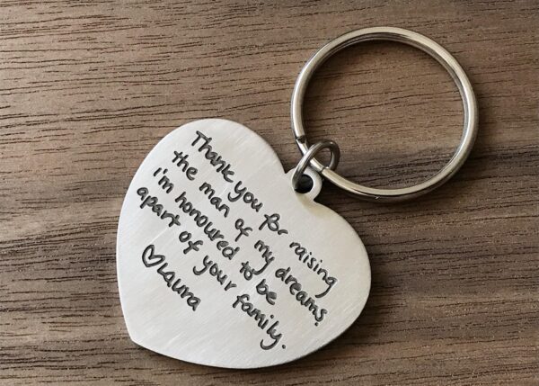 Heart-shaped keychain with engraved message expressing gratitude to a mother-in-law, laid on a wooden surface.