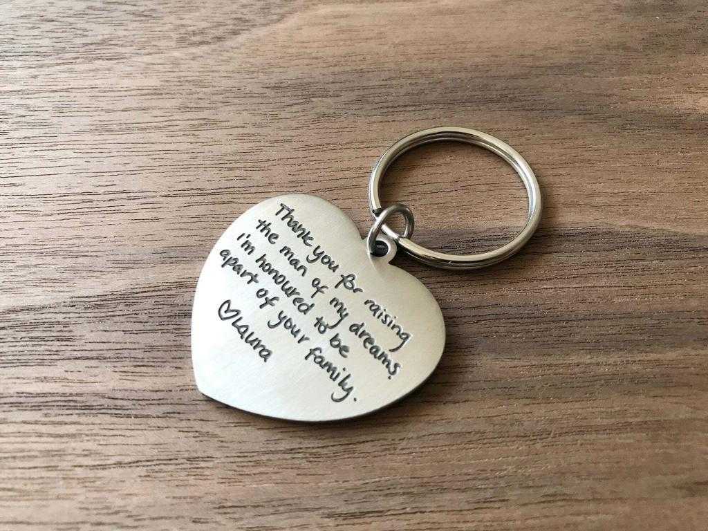 Heart-shaped keychain with engraved message on a wooden surface, expressing gratitude to a parent.