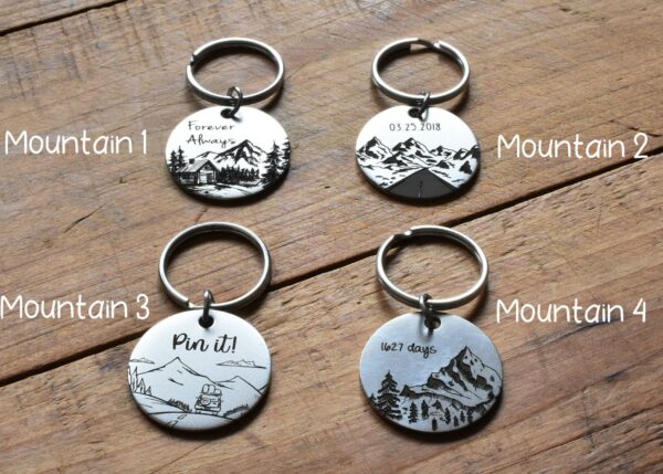 Four engraved mountain-themed keychains on wood surface, labeled Mountain 1 to Mountain 4.