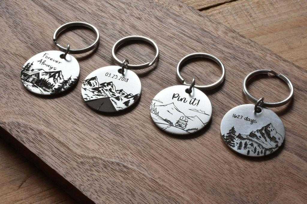 Four engraved round keychains on wooden surface, showcasing scenic mountain designs and custom text.