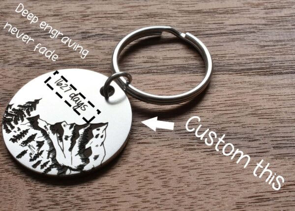 Customizable engraved keychain with mountain design on wooden background. Perfect for personalized gifts.