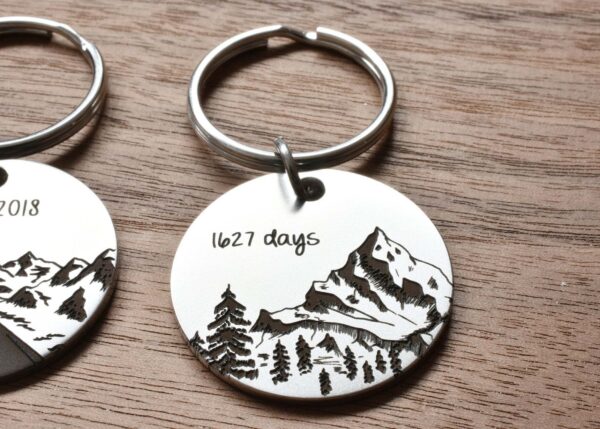 Engraved mountain keychain on wood surface, marked 1627 days, showcasing custom design and craftsmanship.