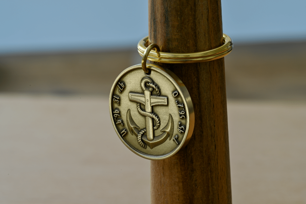 Round brass keychain featuring an anchor wrapped in rope, engraved with geographic coordinates along the edge