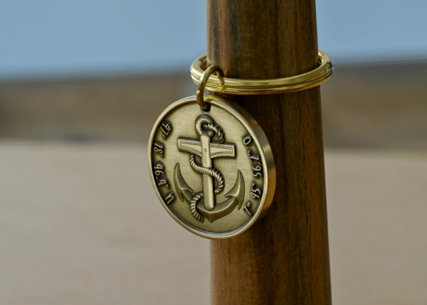 Round brass keychain featuring an anchor wrapped in rope, engraved with geographic coordinates along the edge