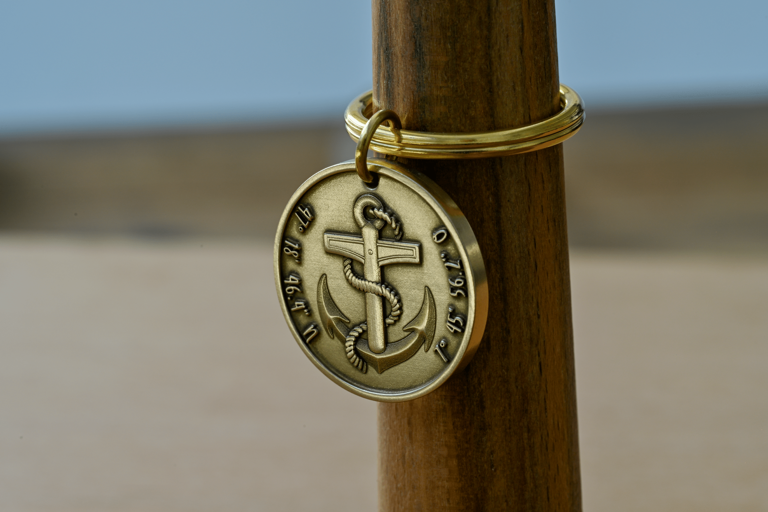 Round brass keychain featuring an anchor wrapped in rope, engraved with geographic coordinates along the edge