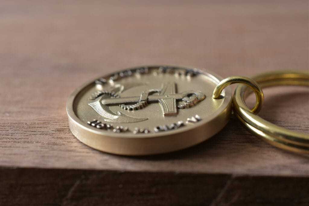 Close-up of a gold keychain with embossed anchor design on wooden background.