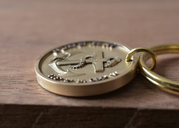 Close-up of a gold keychain with embossed anchor design on wooden background.