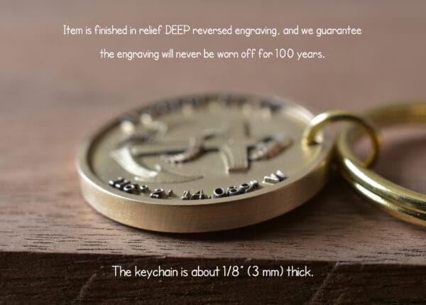 Close-up of a gold keychain with deep engraved design, guaranteed for 100 years, 1/8 inch thick on wooden surface.