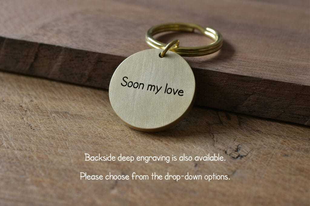 Gold keychain with Soon my love engraving on rustic wooden background. Backside deep engraving available.