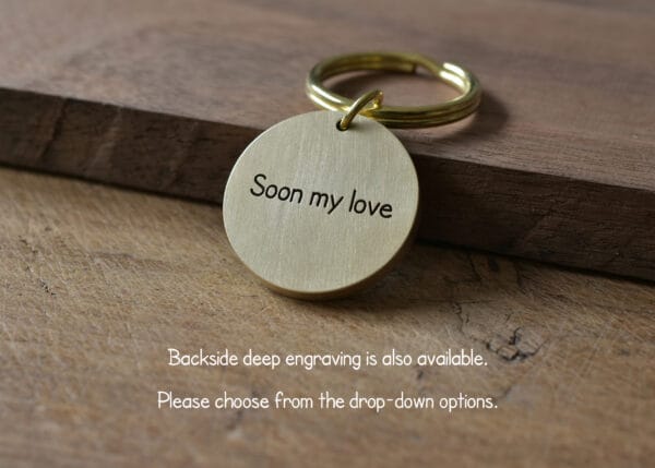 Gold keychain with Soon my love engraving on rustic wooden background. Backside deep engraving available.