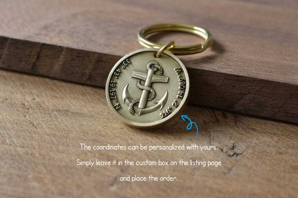 Personalized keychain with anchor design and customizable GPS coordinates on a wooden surface.