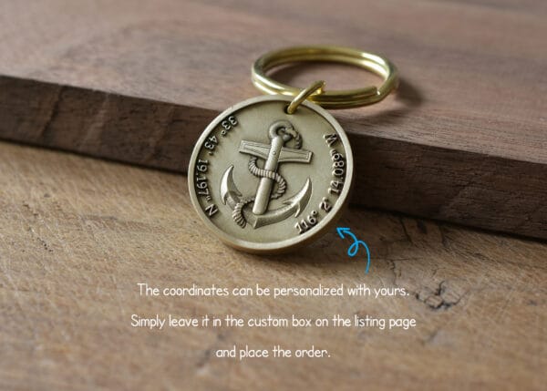 Personalized keychain with anchor design and customizable GPS coordinates on a wooden surface.