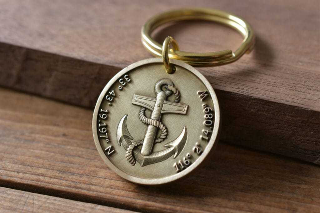 Gold keyring with engraved anchor and coordinates, resting on wooden surface, symbolizes nautical themes and travel.