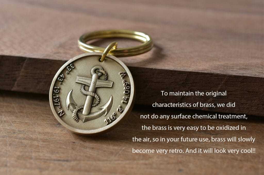 Brass anchor keychain with engraved coordinates, placed on a wooden surface.