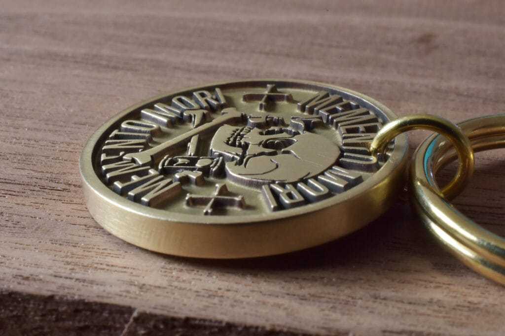 Close-up of a brass memento mori coin with engraved skull on a wooden surface.