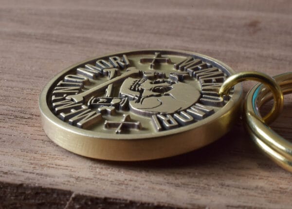 Close-up of a brass memento mori coin with engraved skull on a wooden surface.