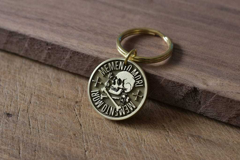 Gold Memento Mori keychain with skull engraving on a wooden surface.