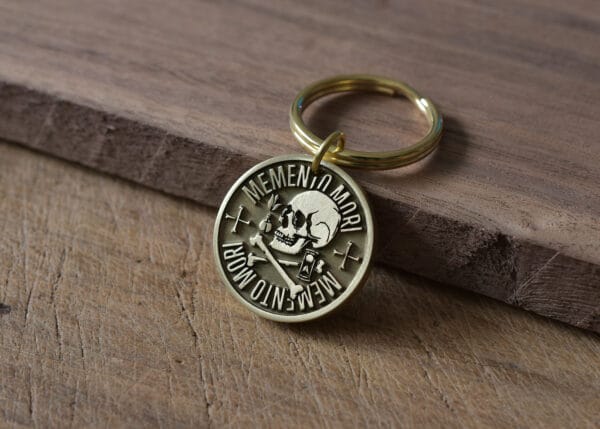 Gold Memento Mori keychain with skull engraving on a wooden surface.