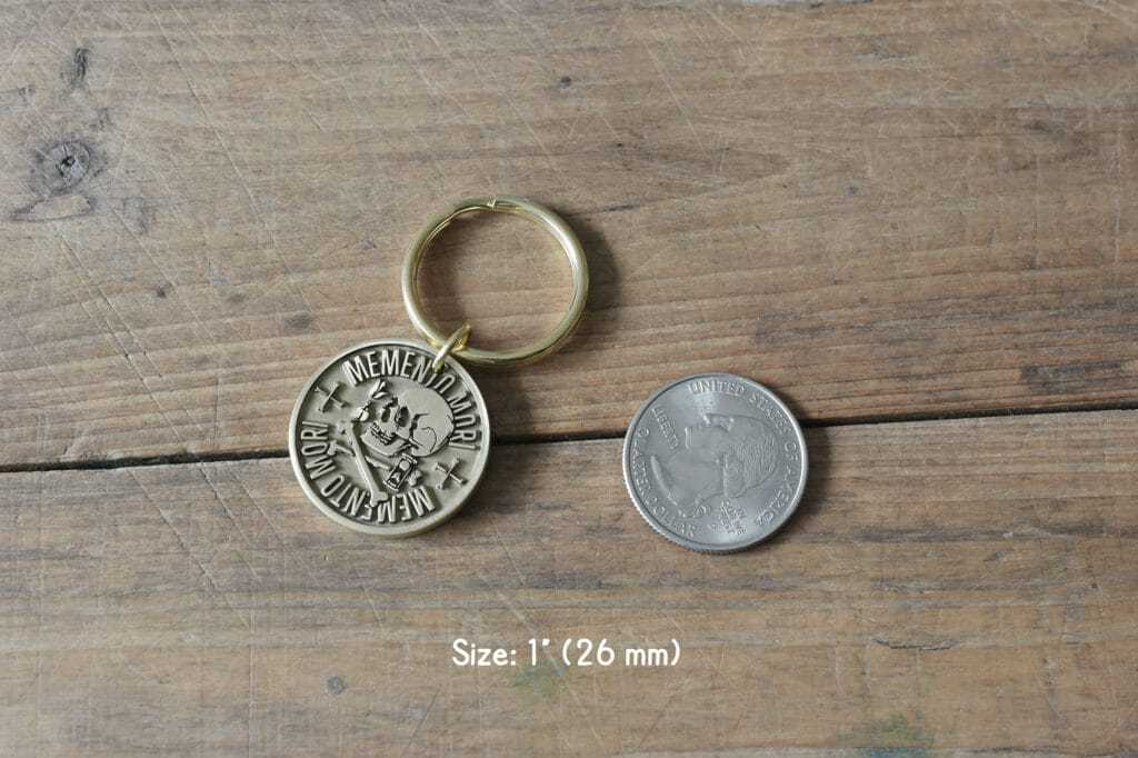 Memento Mori skull keychain next to a quarter on wooden surface, 1-inch diameter (26mm).