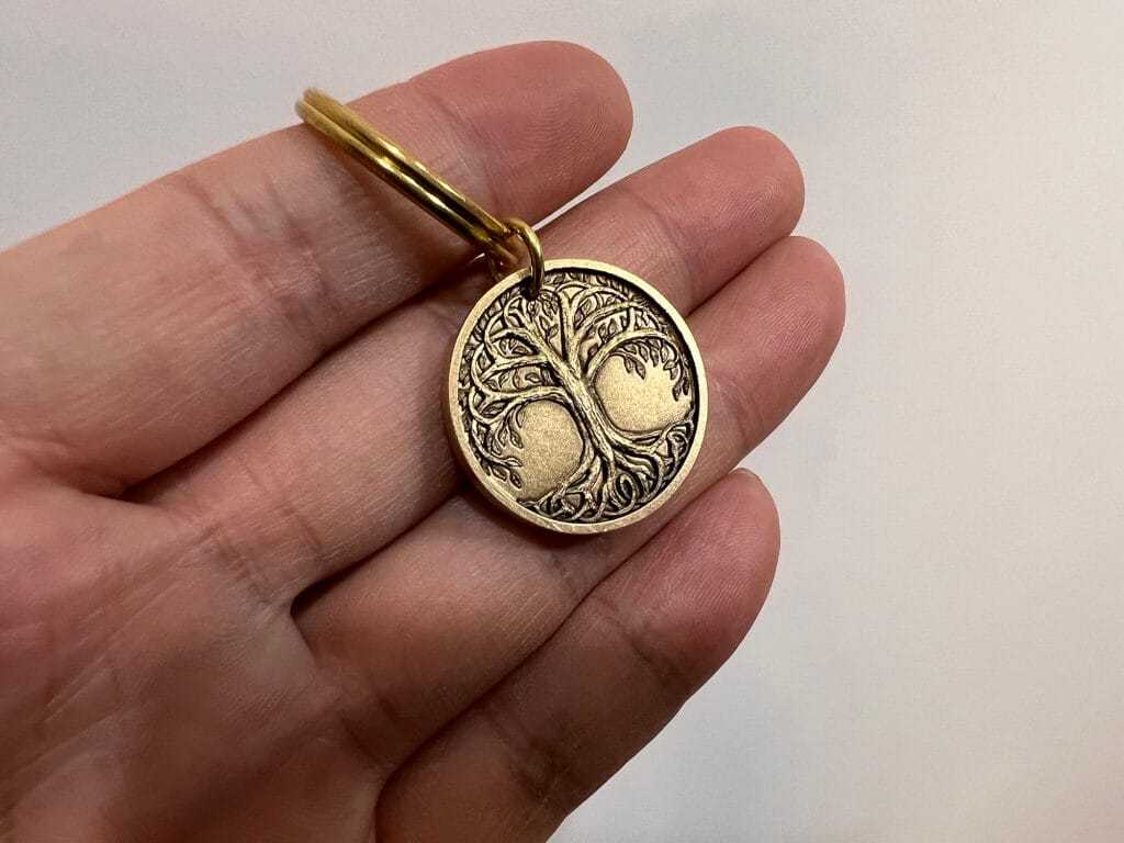 Hand holding a round bronze keychain with a detailed tree engraving, symbolizing connection and growth.