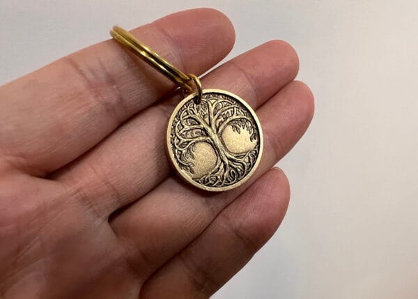 Hand holding a round bronze keychain with a detailed tree engraving, symbolizing connection and growth.