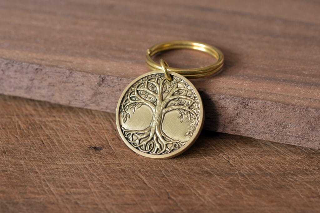 Gold tree of life keychain on wooden surface, symbolizing growth and strength.