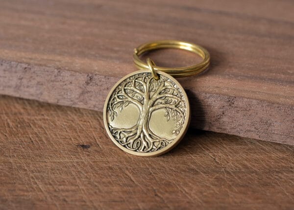 Gold tree of life keychain on wooden surface, symbolizing growth and strength.