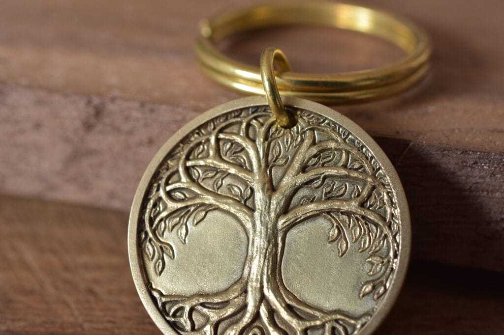 Gold keychain with engraved tree of life emblem on a wooden surface.