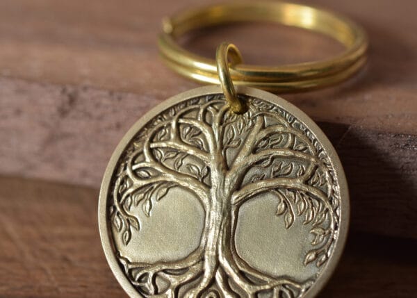 Gold keychain with engraved tree of life emblem on a wooden surface.