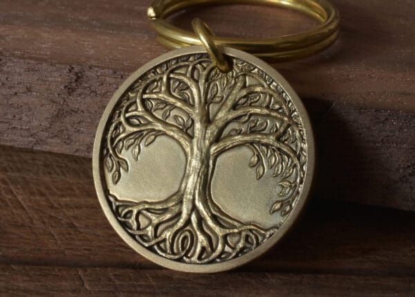 Golden Tree of Life pendant keyring on wooden background, symbolizing growth and strength.