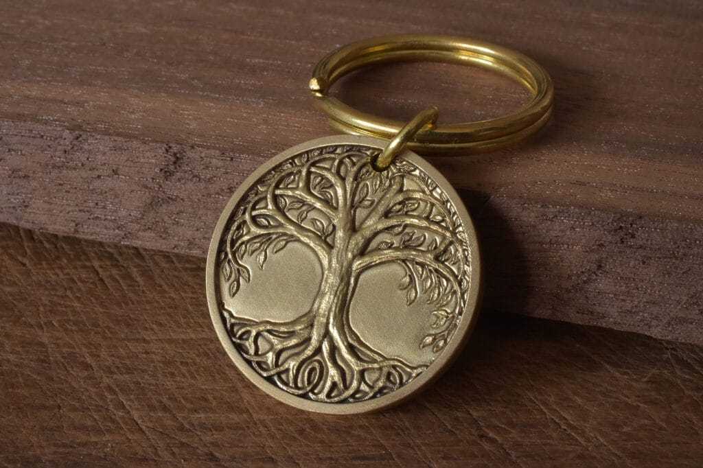 Gold tree of life keychain on wooden surface, intricate design, symbolizing growth and connection.