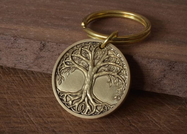 Gold tree of life keychain on wooden surface, intricate design, symbolizing growth and connection.