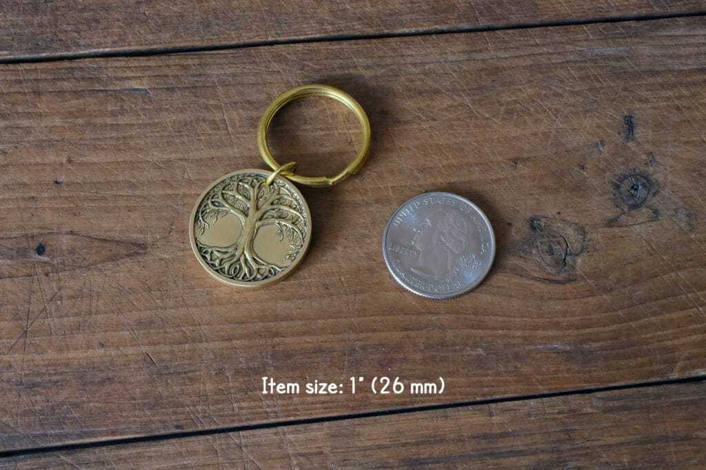 Gold tree of life keychain beside quarter for size comparison, on wooden table. Keychain size: 1 inch (26 mm).
