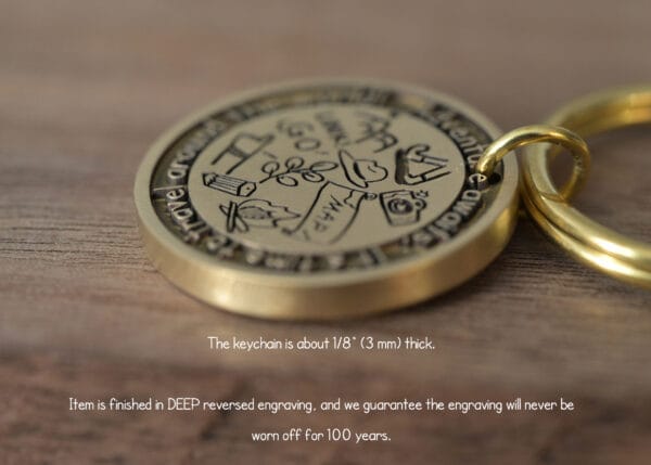Close-up of a gold keychain with deep engraving, showcasing travel-themed icons on a wooden surface.