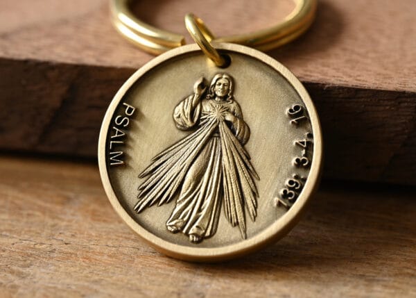 Gold religious medallion featuring a figure and inscribed with Psalm 139:3-4,16 on a wooden surface.