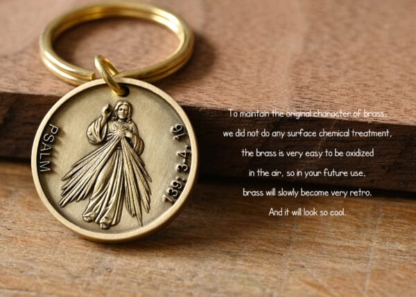 Brass keychain with religious engraving on a wooden surface, highlighting its natural oxidation process for a vintage look.