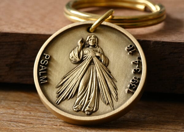 Bronze religious medallion featuring a figure with rays, Psalm text, and keyring on wood surface.