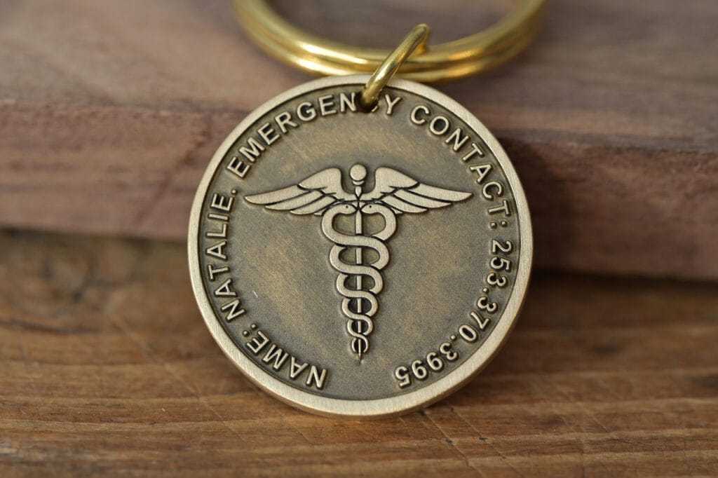 Close-up of a metal keychain featuring a caduceus symbol and engraved emergency contact details.