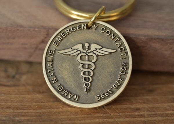 Close-up of a metal keychain featuring a caduceus symbol and engraved emergency contact details.