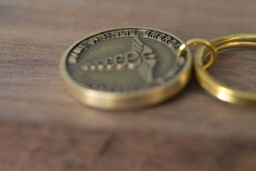 Close-up of a gold medical alert keychain on a wooden surface, engraved with a caduceus symbol and text.